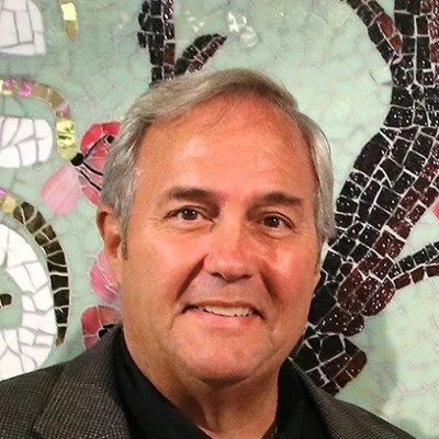 Portrait of a middle-aged man with gray hair smiling in front of a colorful mosaic background.