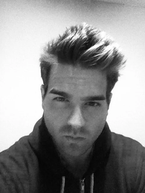 Black and white photo of a young man with styled hair, wearing a hoodie.