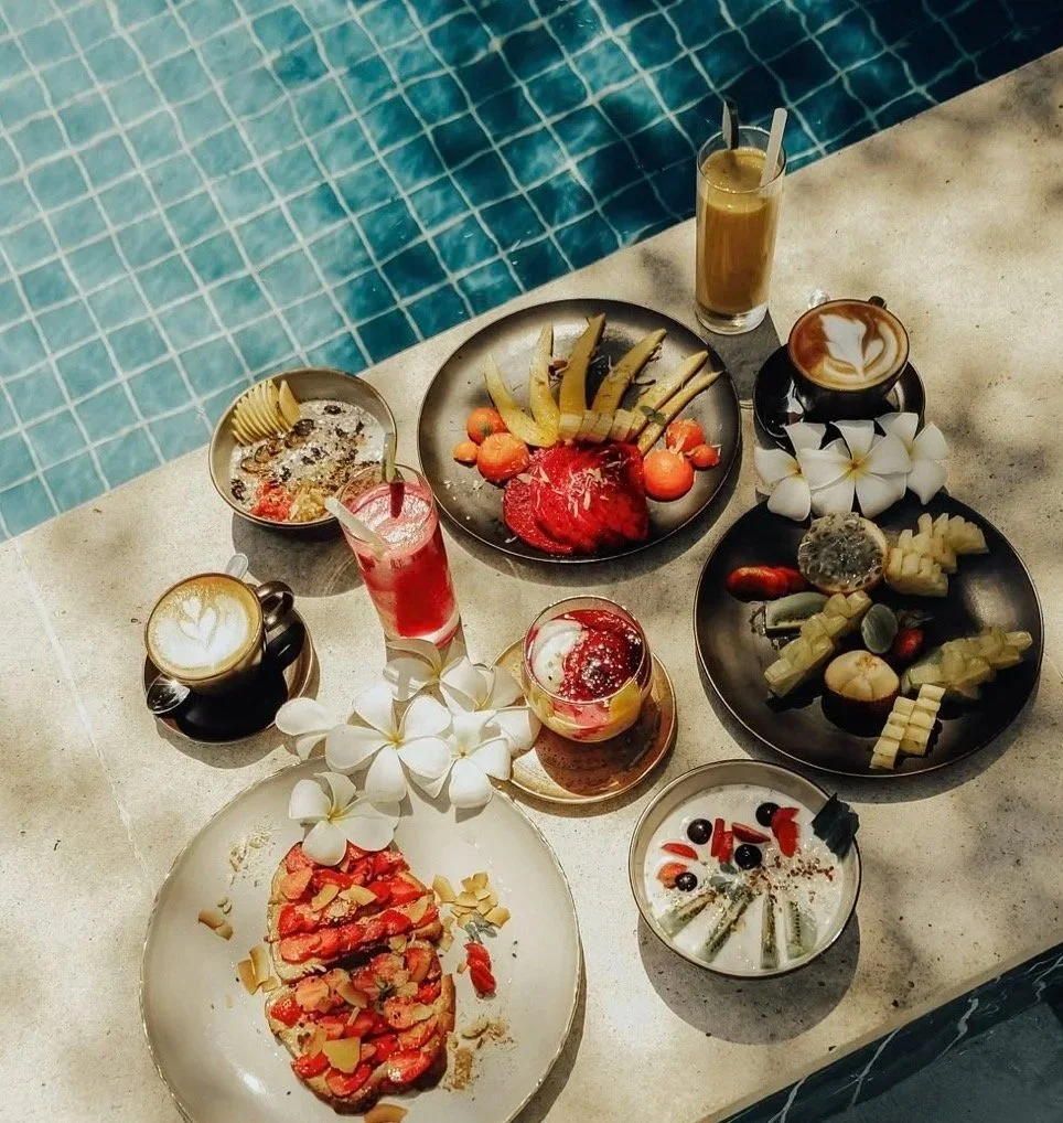 Assorted desserts, fruits, and beverages arranged on a poolside table with a swimming pool in the background.