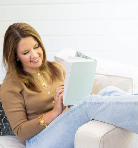A woman sitting on a couch reading a book, smiling.