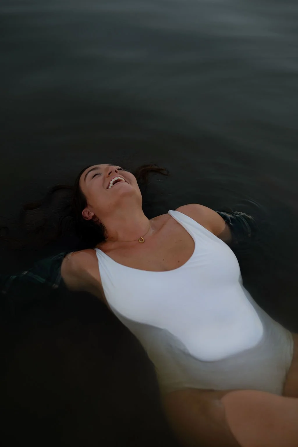 Woman lying in dark water, smiling and looking up