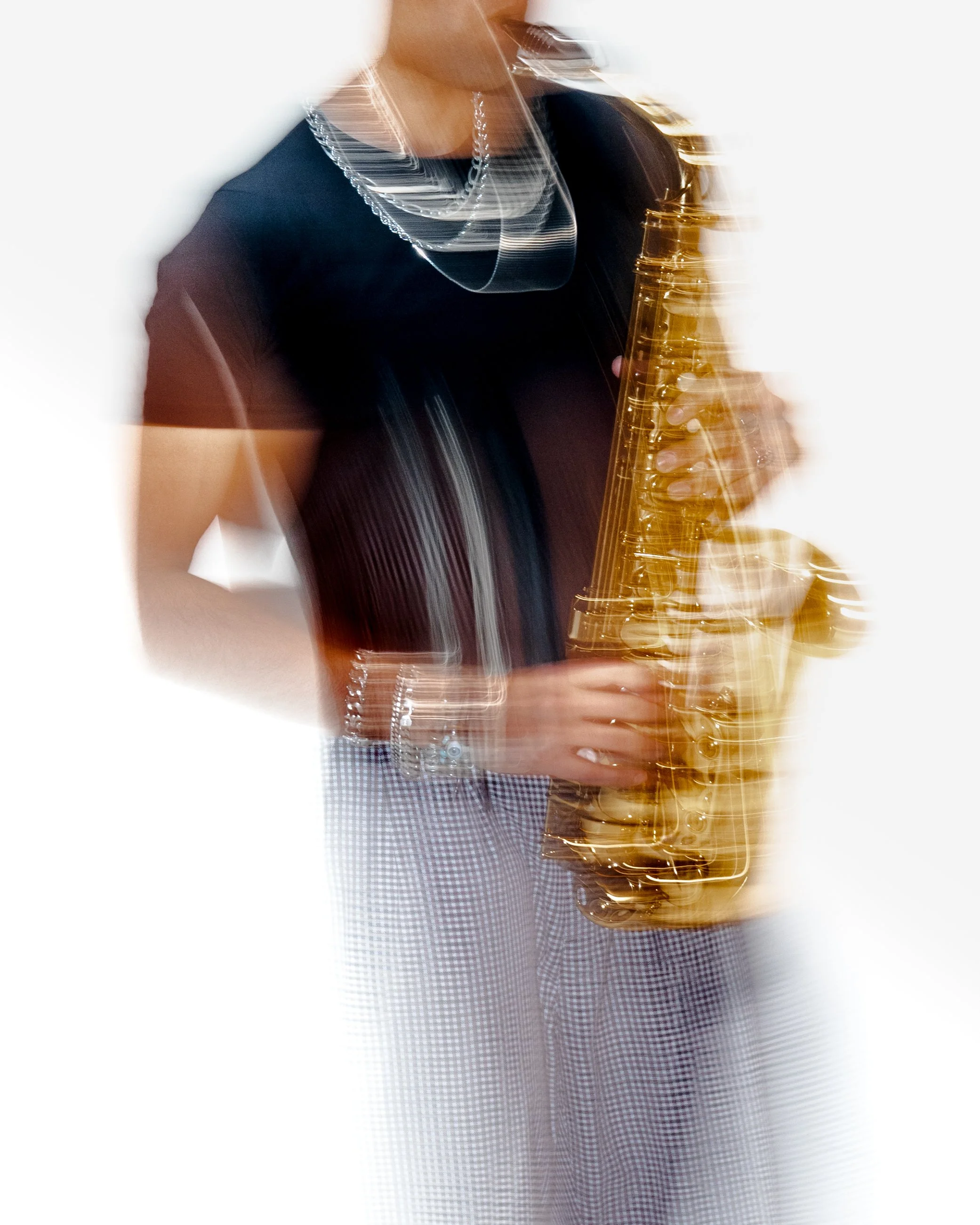Person playing a saxophone, wearing a black shirt, with jewelry, and holding a saxophone, against a blurred background with streaks of motion.