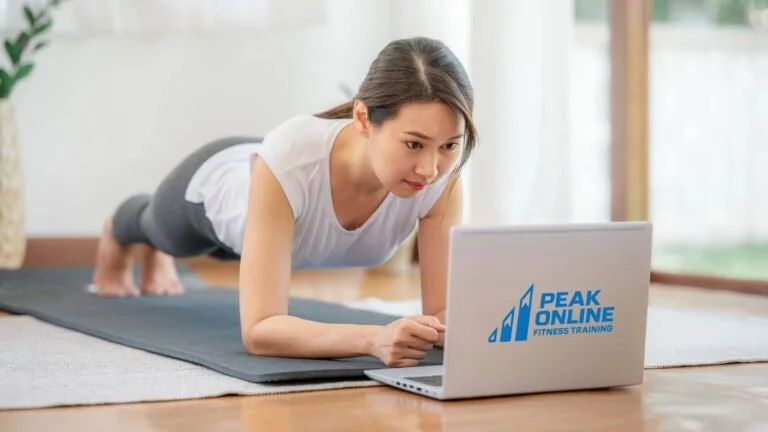Woman doing push-ups on a yoga mat at home, watching a fitness training video on her laptop.