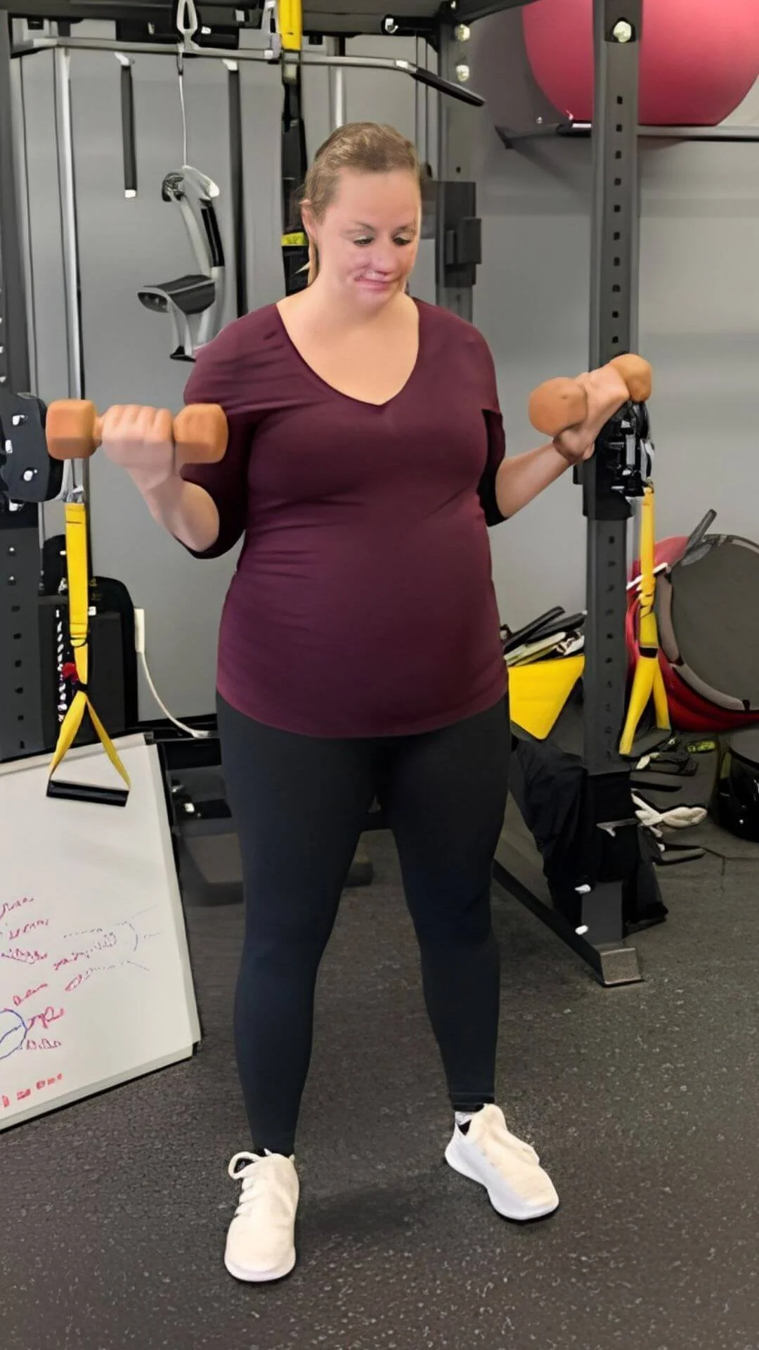 A woman in workout clothes lifting dumbbells in a gym.