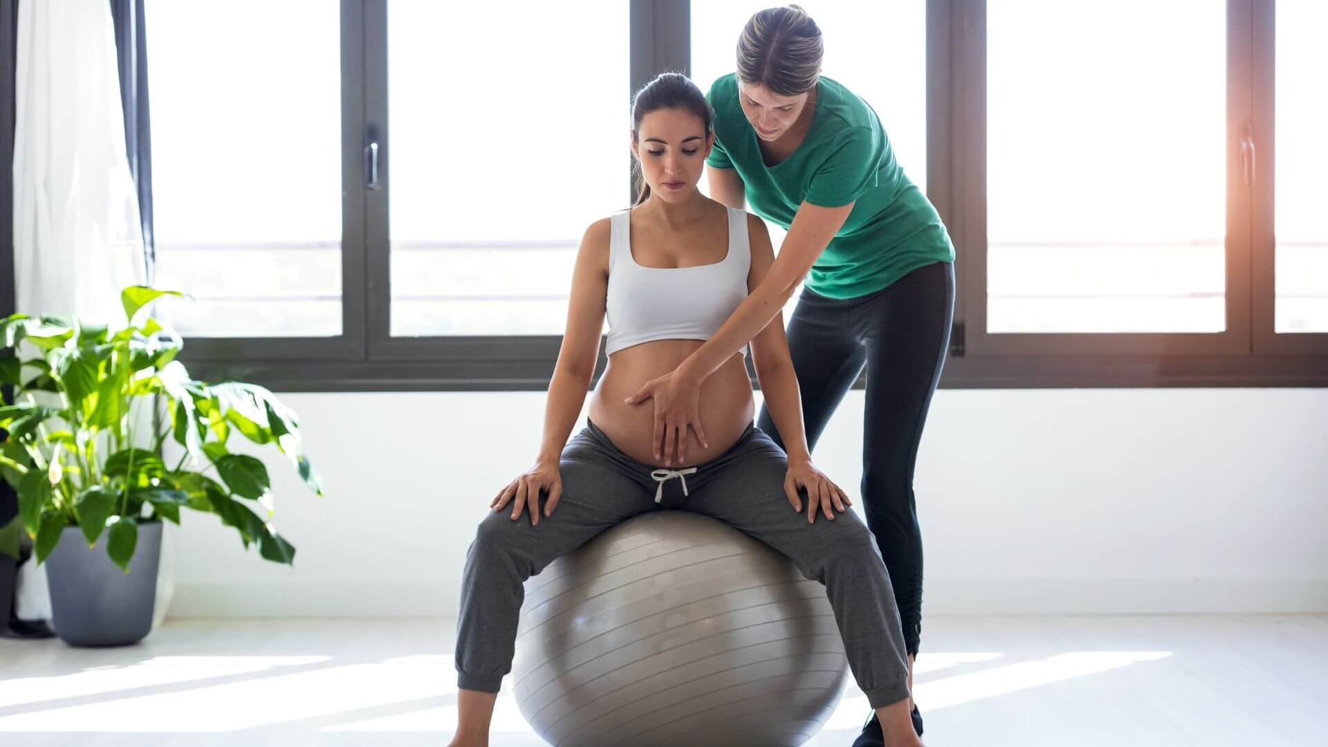 a personal trainer holding a pregnant womans belly while helping her exercise
