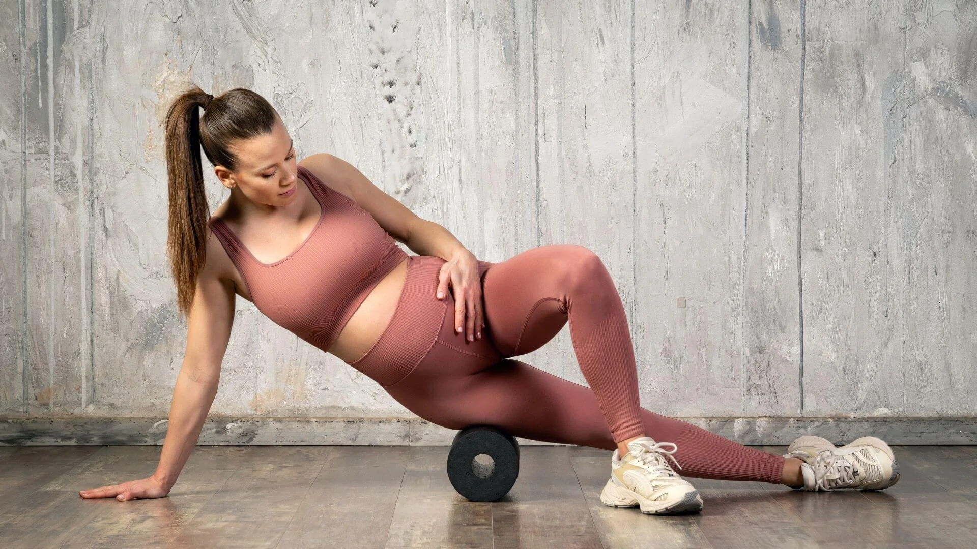 pregnant woman holding her belly while foam rolling her hip
