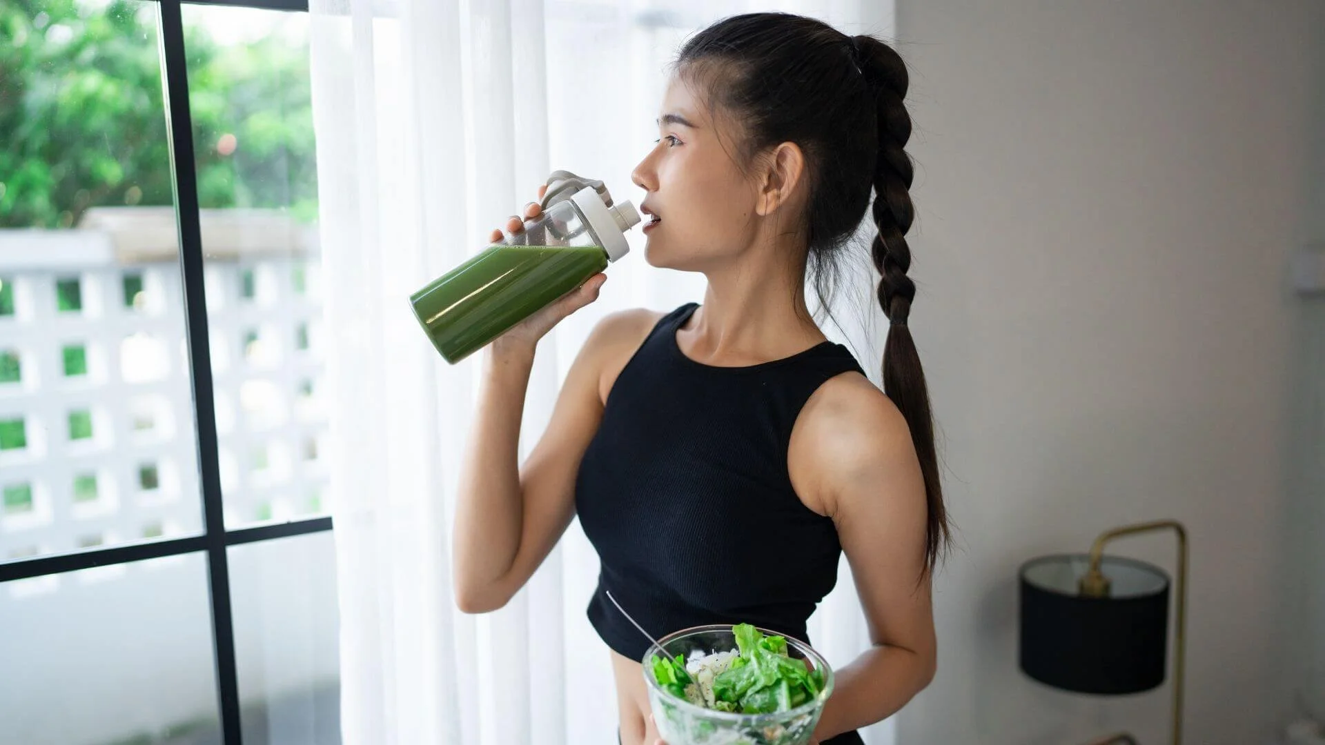 woman drinking a healthy smoothie while holding a salad