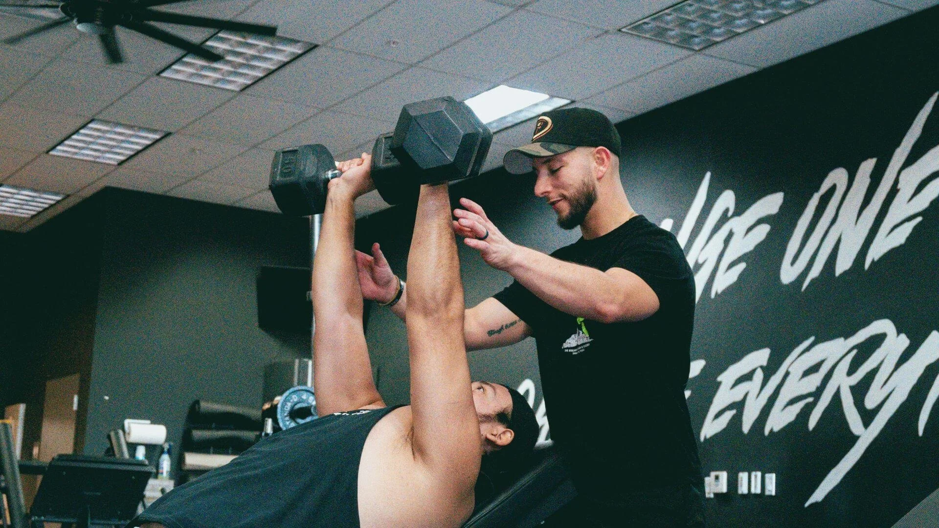 man lifting weights while being spotted by his personal trainer