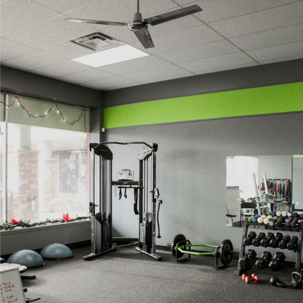 An empty fitness room with gym equipment, weights, and a large window with holiday lights.