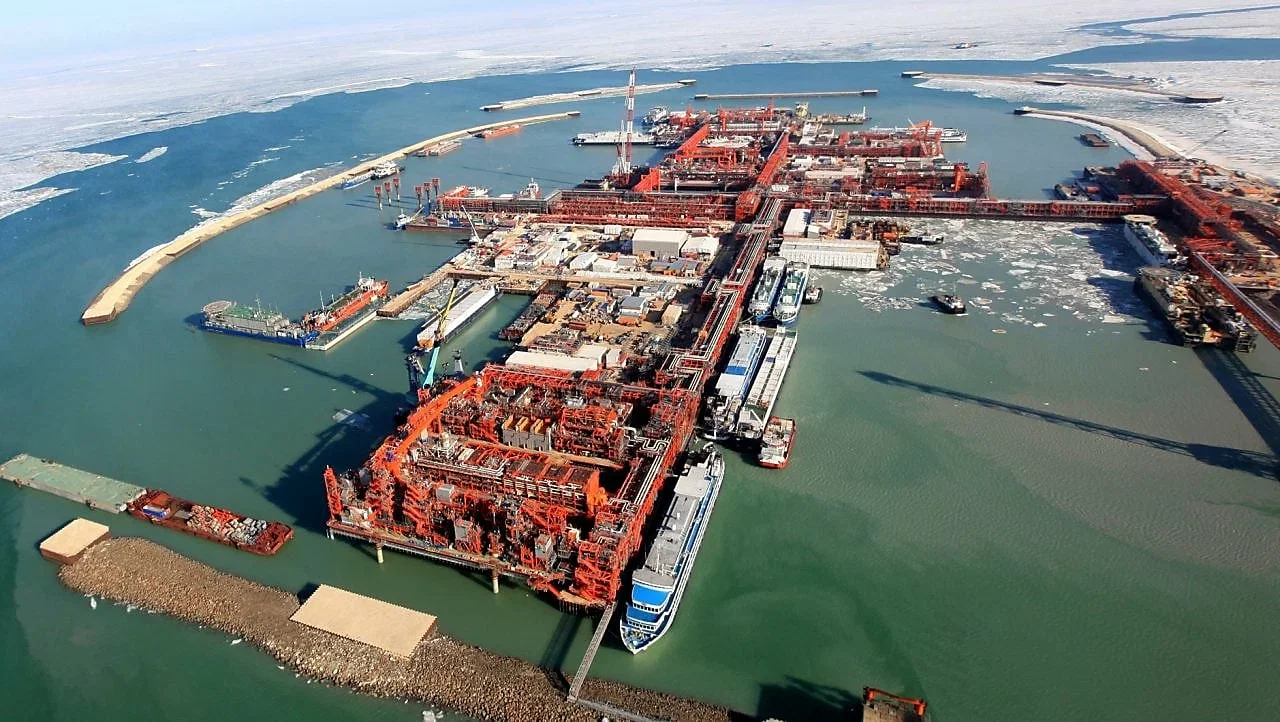 Shell Kazakhstan B.V Aerial view of an industrial drilling port with large ships, cranes, and infrastructure, surrounded by icy waters and snow-covered land.