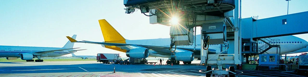 View of aircraft at an airport gate with jet bridges and ground crew equipment during daylight.