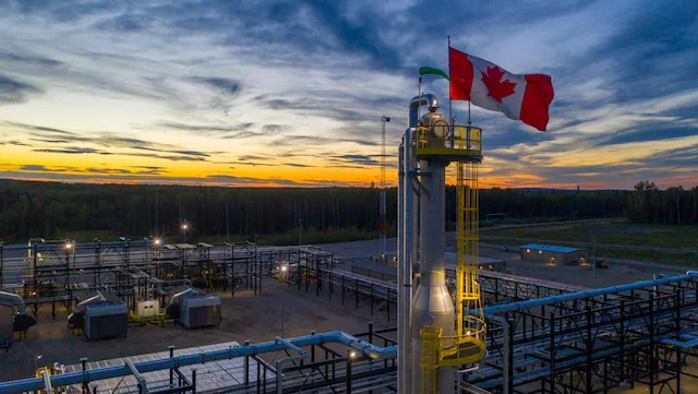 Oil refinery with pipelines, a tall distillation column, and a Canadian flag flying at sunset.