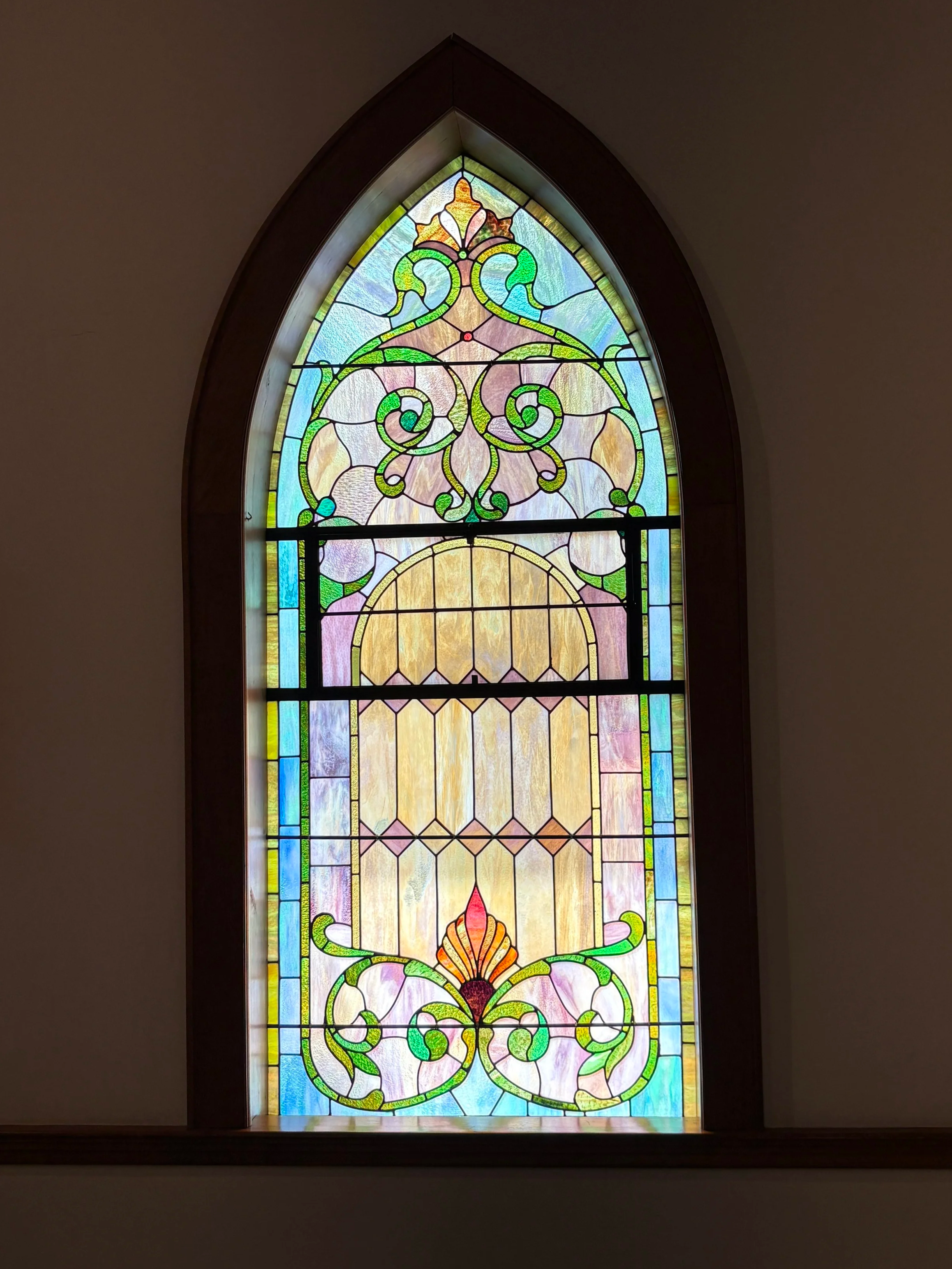 Colorful stained glass window with intricate floral and abstract design, framed in wood, set in a wall.