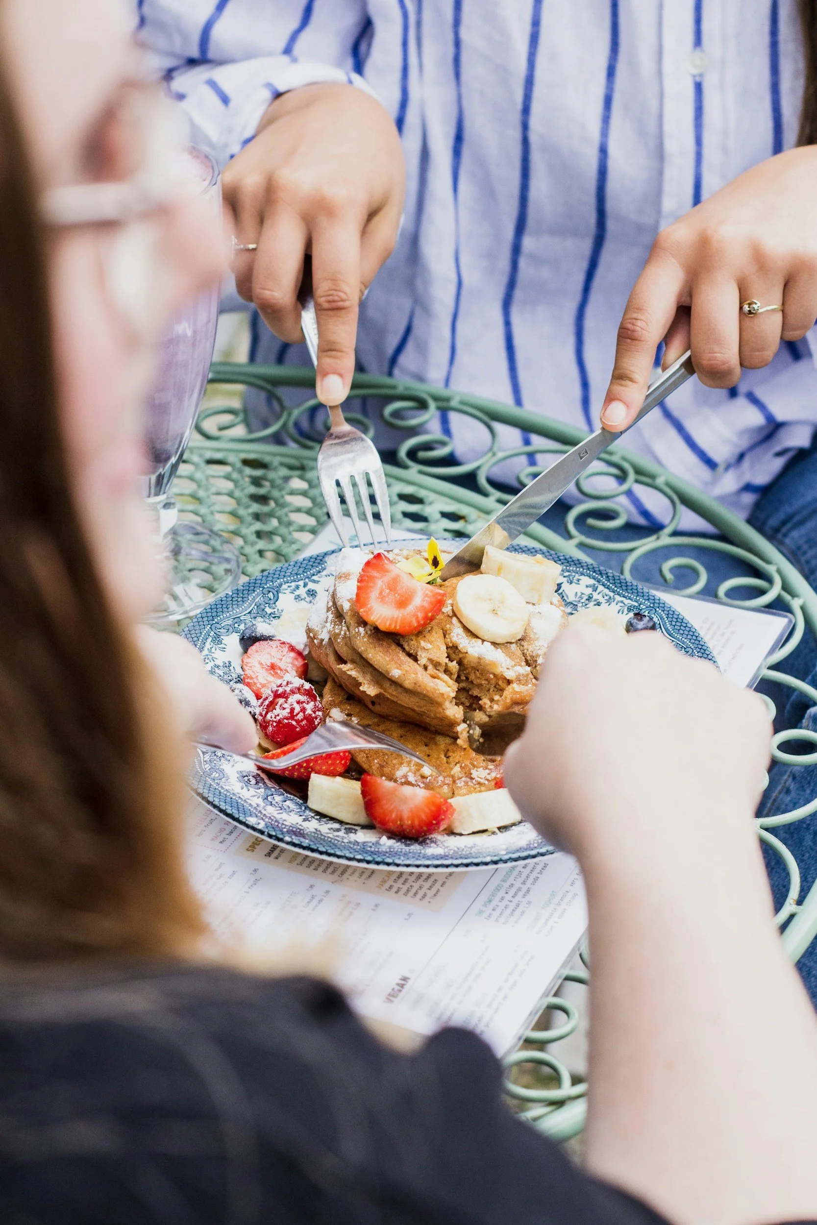 People eating a dessert topped with strawberries and bananas at an outdoor table.