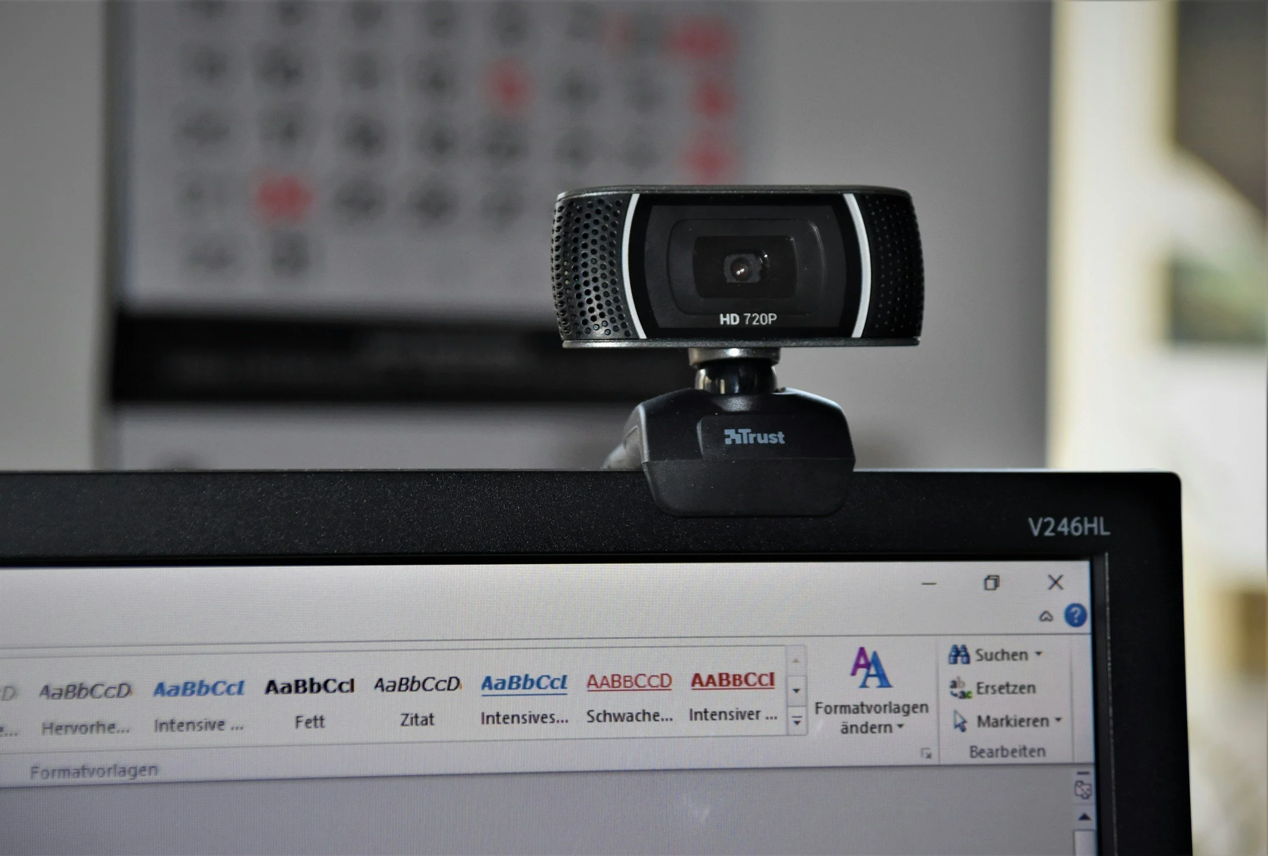 A webcam mounted on a computer monitor in front of a computer screen displaying a text editing program with various font styles and options.