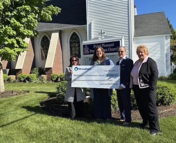 Group of four people standing on grass holding a large check in front of a church building.