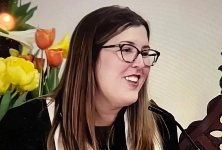 A woman with brown hair, glasses, and a black and white shirt, smiling, with colorful tulips in the background.