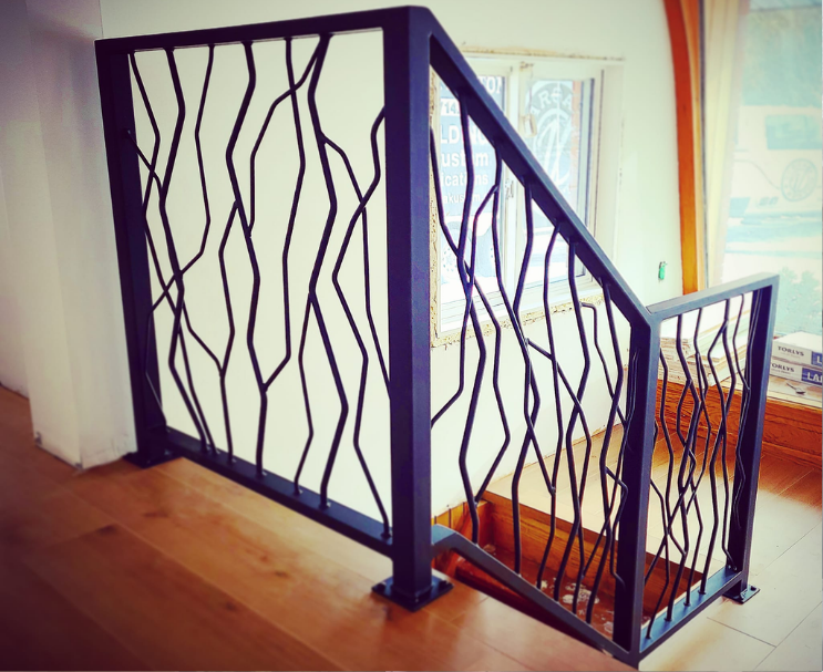Decorative black metal staircase railing with abstract irregular lines, next to a wooden staircase and window.