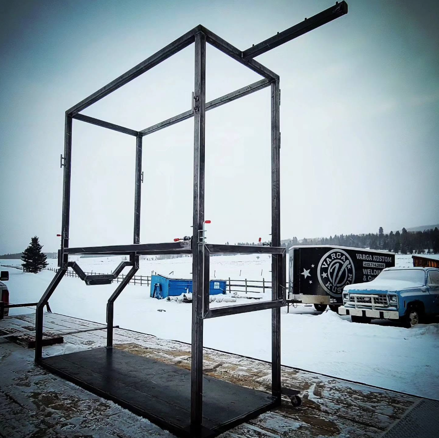 Metal framework structure outdoors in a snowy landscape, with a truck and trailers in the background.