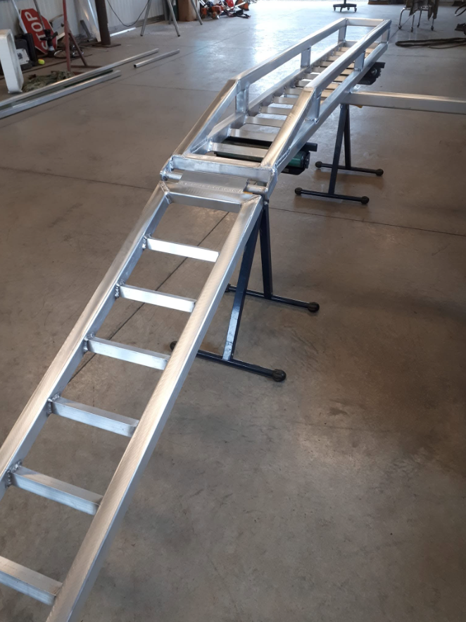 Metal ramp with steps on one side, set up in a workshop or garage with various tools and equipment in the background.