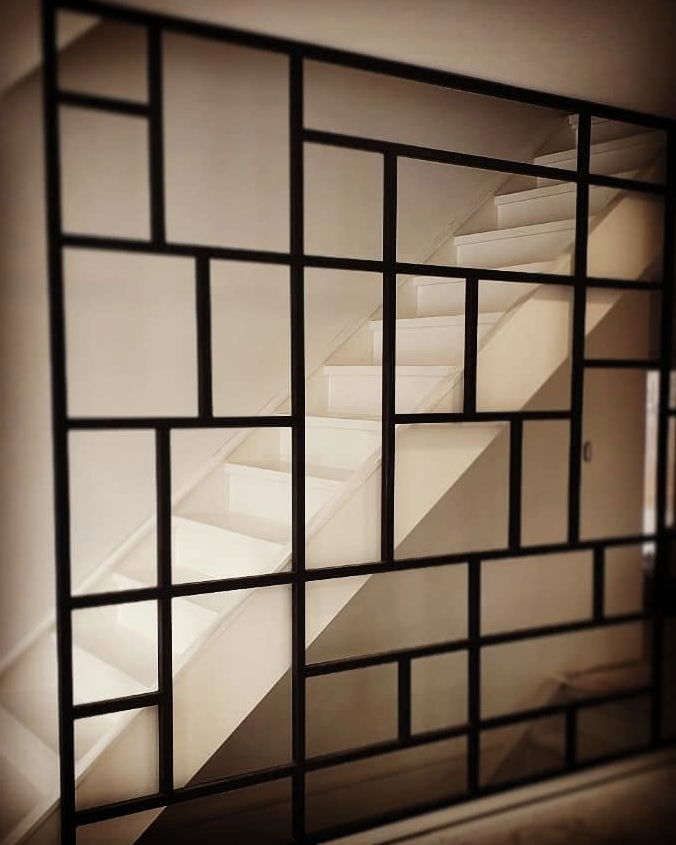 View of a staircase through a decorative black metal grid with geometric patterns.