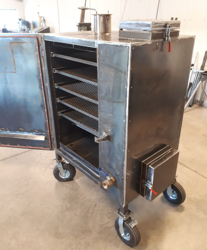 A stainless steel smoker or oven on wheels with multiple racks inside and control valves on the outside, situated in a workshop or industrial space.