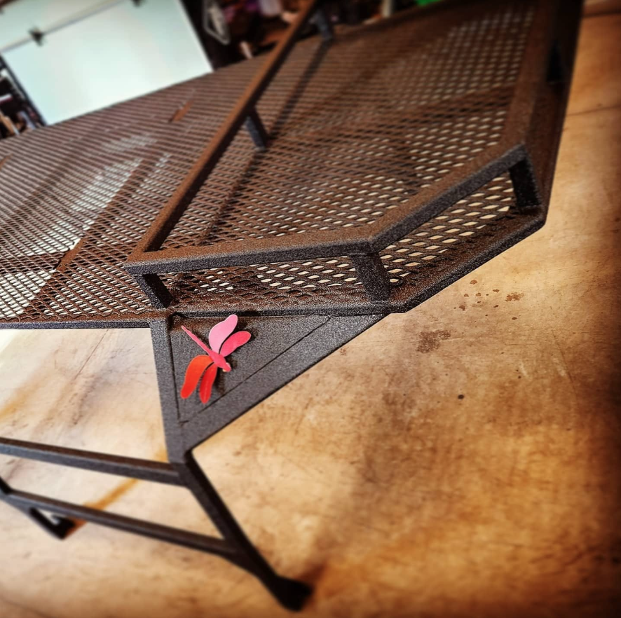 A black metal mesh table with a decorative pink and red butterfly on one corner, placed on a wooden surface.