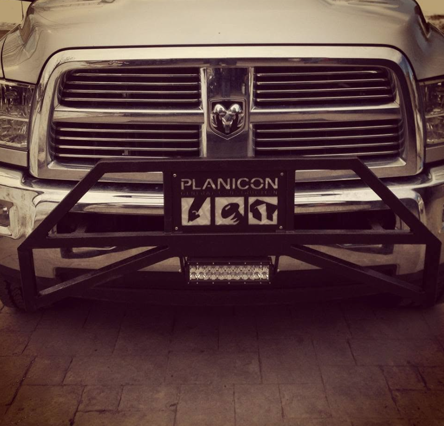 Front of a silver pickup truck with a black metal bumper and a license plate that reads 'PLANICON.' There is a Dodge emblem on the grille.
