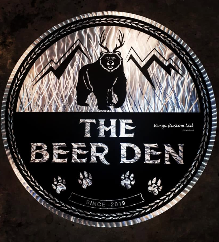 A circular sign with a bear, mountain, and lightning bolt design, reading 'The Beer Den,' with a paw print motif and the text 'Since 2019' and 'Varga Kustom Ltd' in a smaller font.