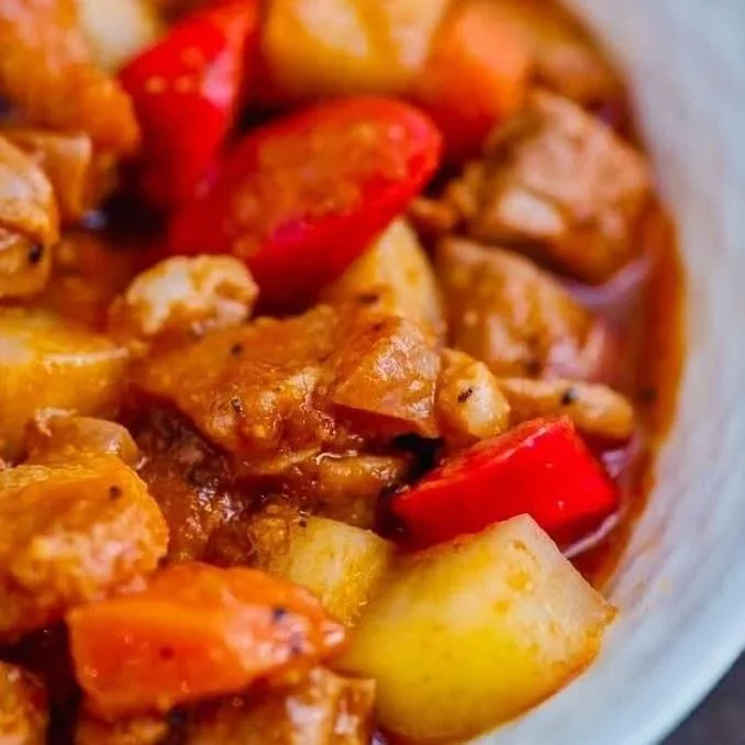 Close-up of a bowl of beef curry with potatoes, carrots, and red bell peppers.