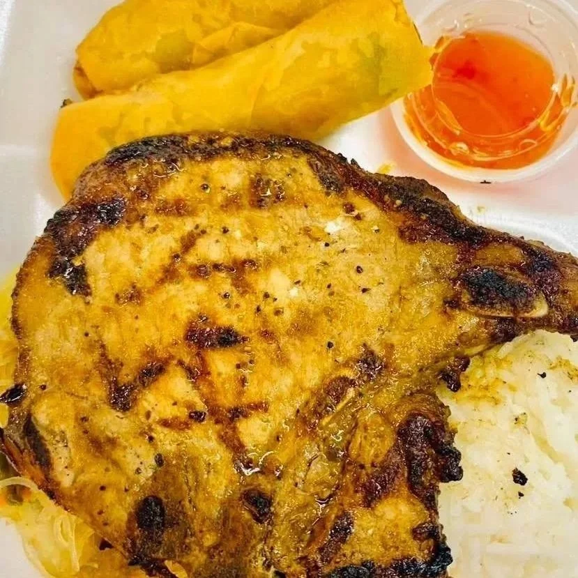 Grilled chicken thigh with golden turmeric rice, fried plantains, white rice, and a small bowl of chili sauce.