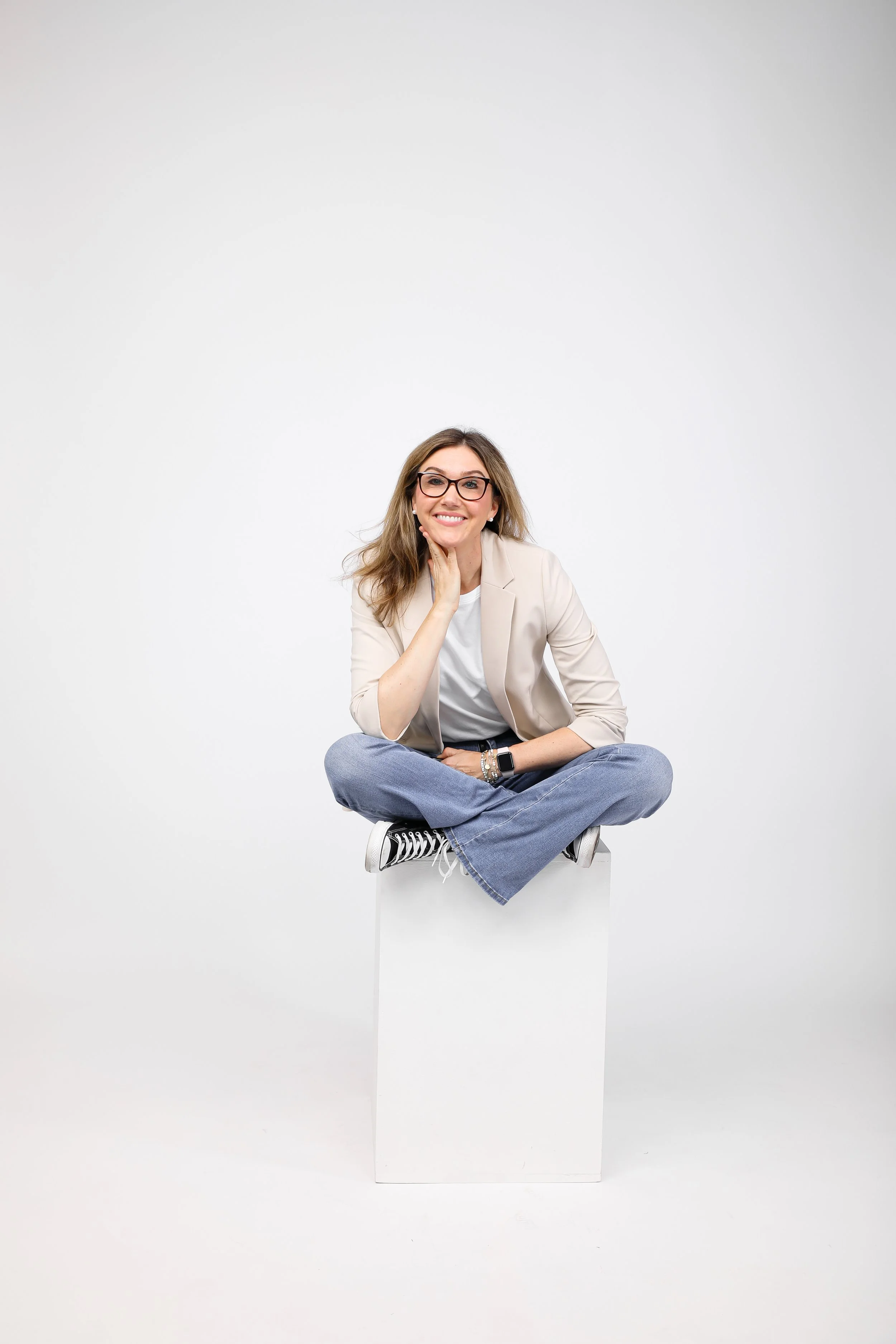 Headshot of author and CEO Jamie Moraga sitting cross‑legged, wearing glasses, with her hand resting on her chin