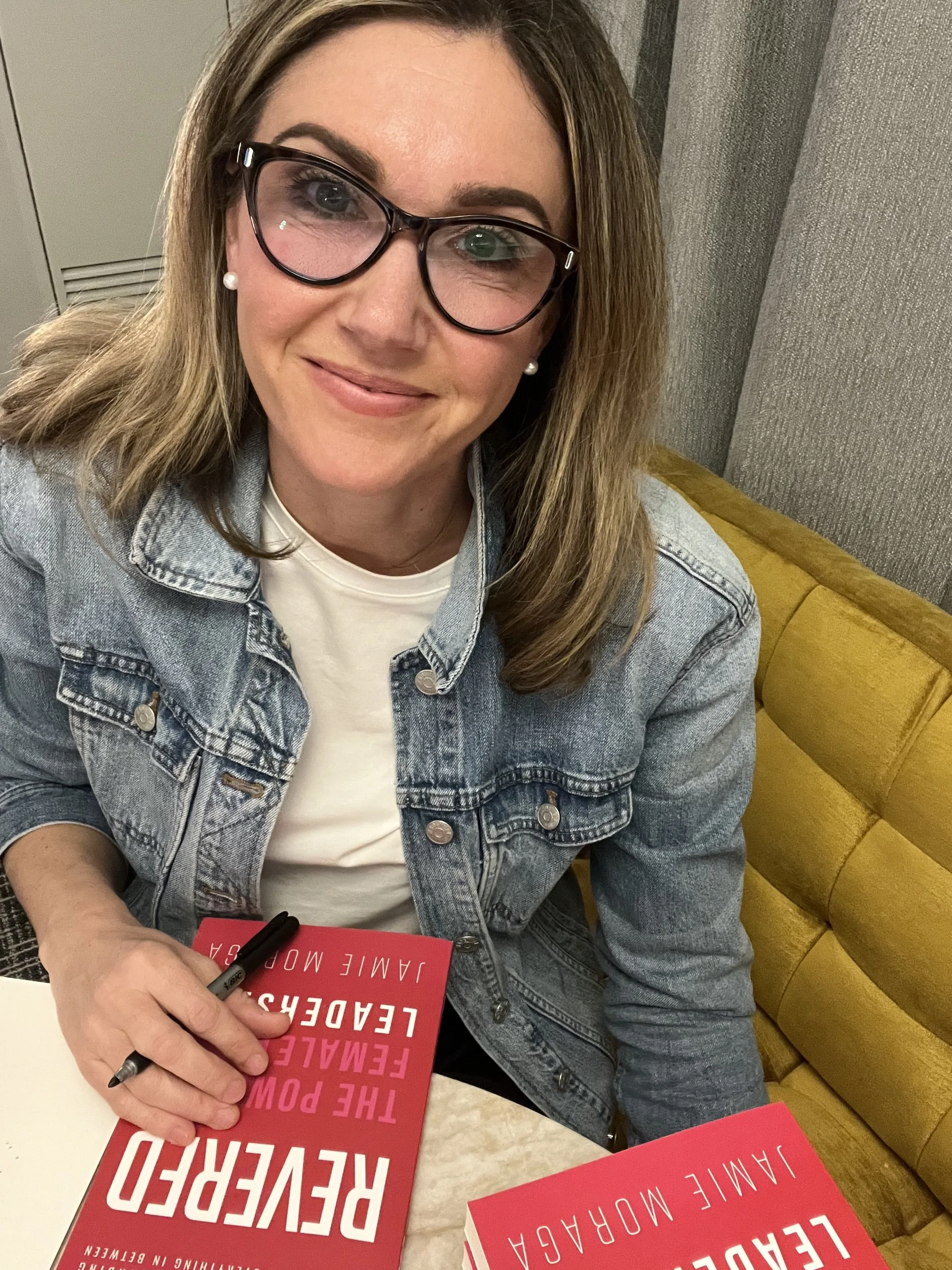 Author and CEO Jamie Moraga smiling at camera while signing her book REVERED: The Power of Female Leadership