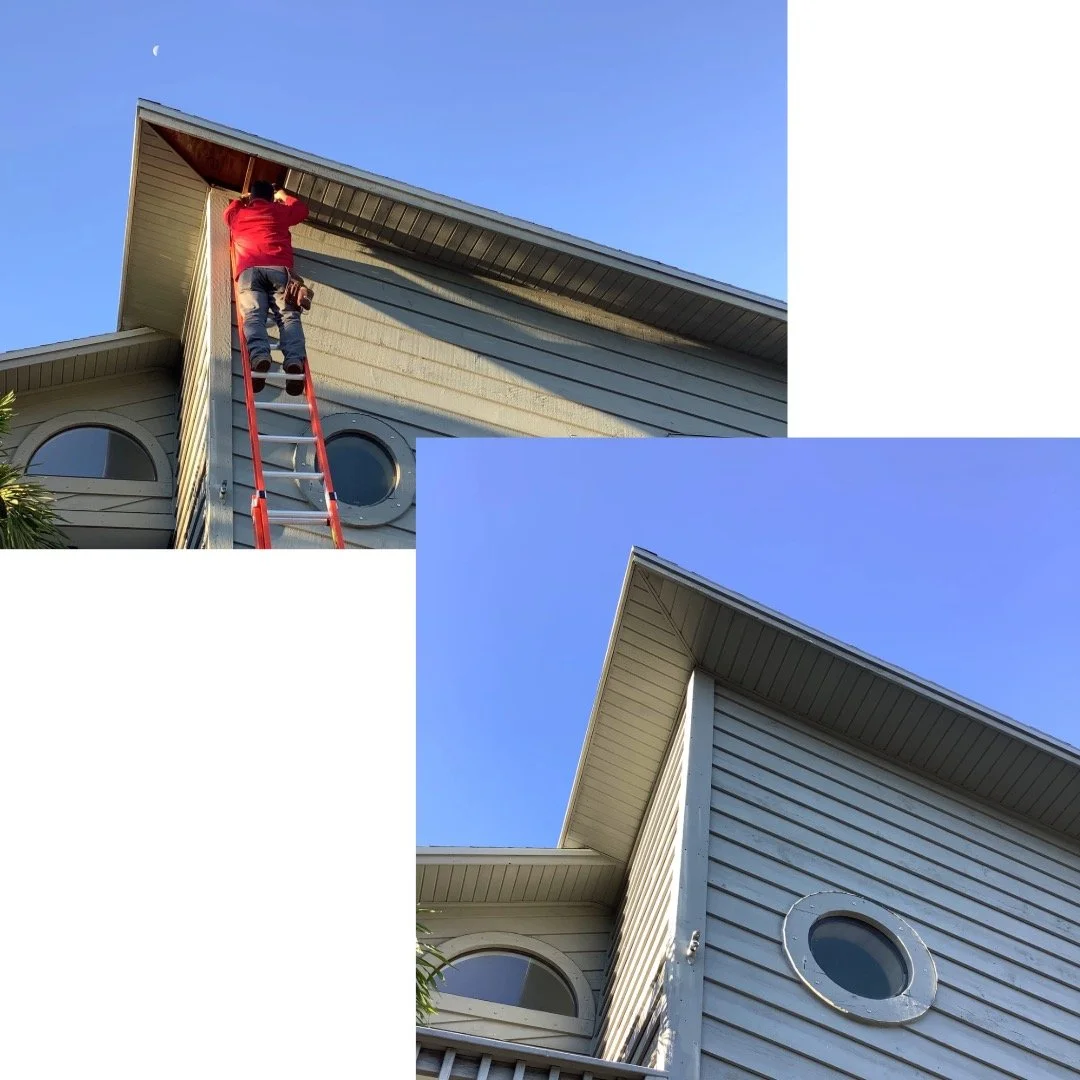 Technician on ladder performing soffit repair on two-story home with blue siding and round windows.