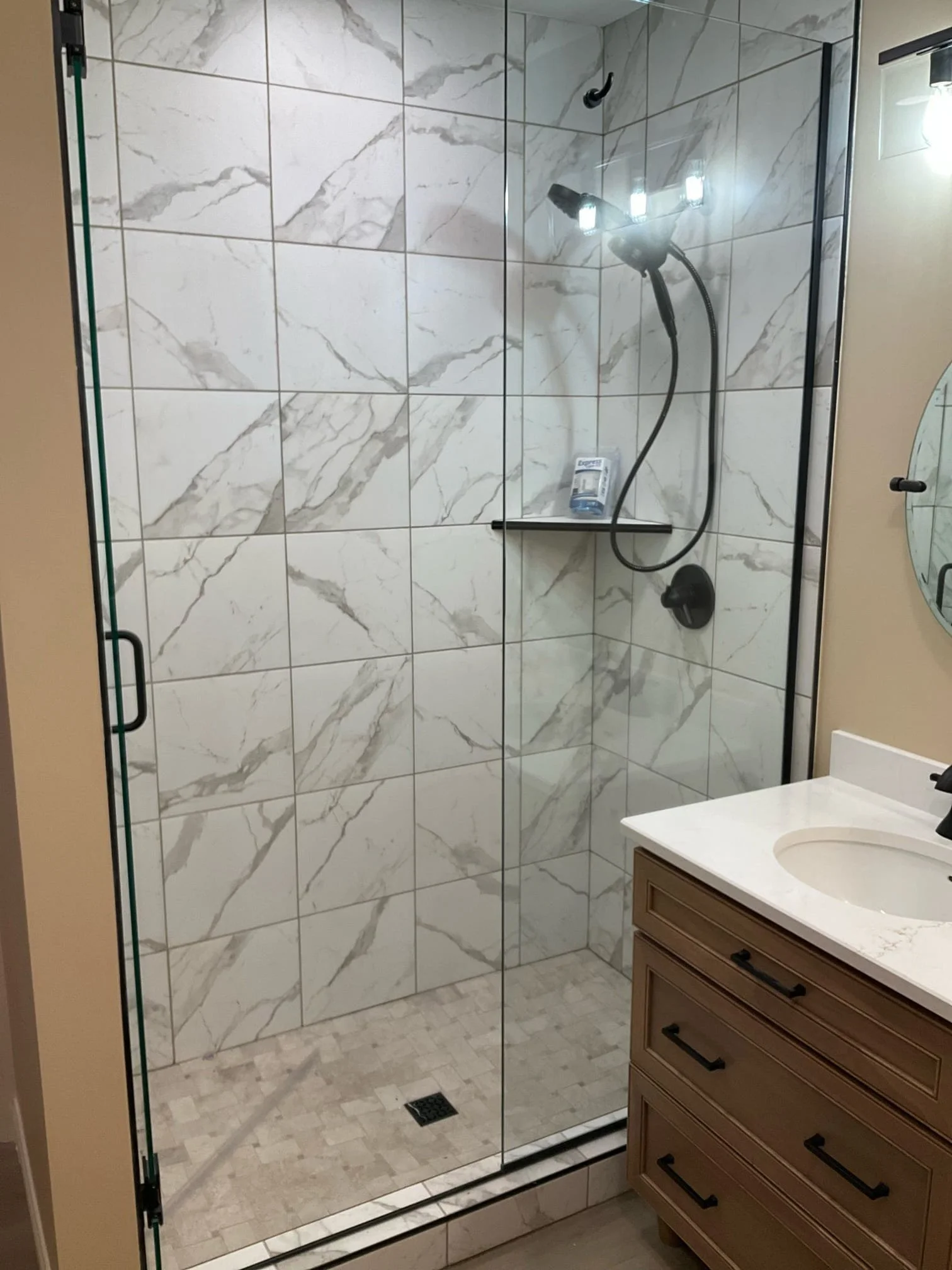 Frameless glass shower with large-format marble-look tiles and matte black hardware.