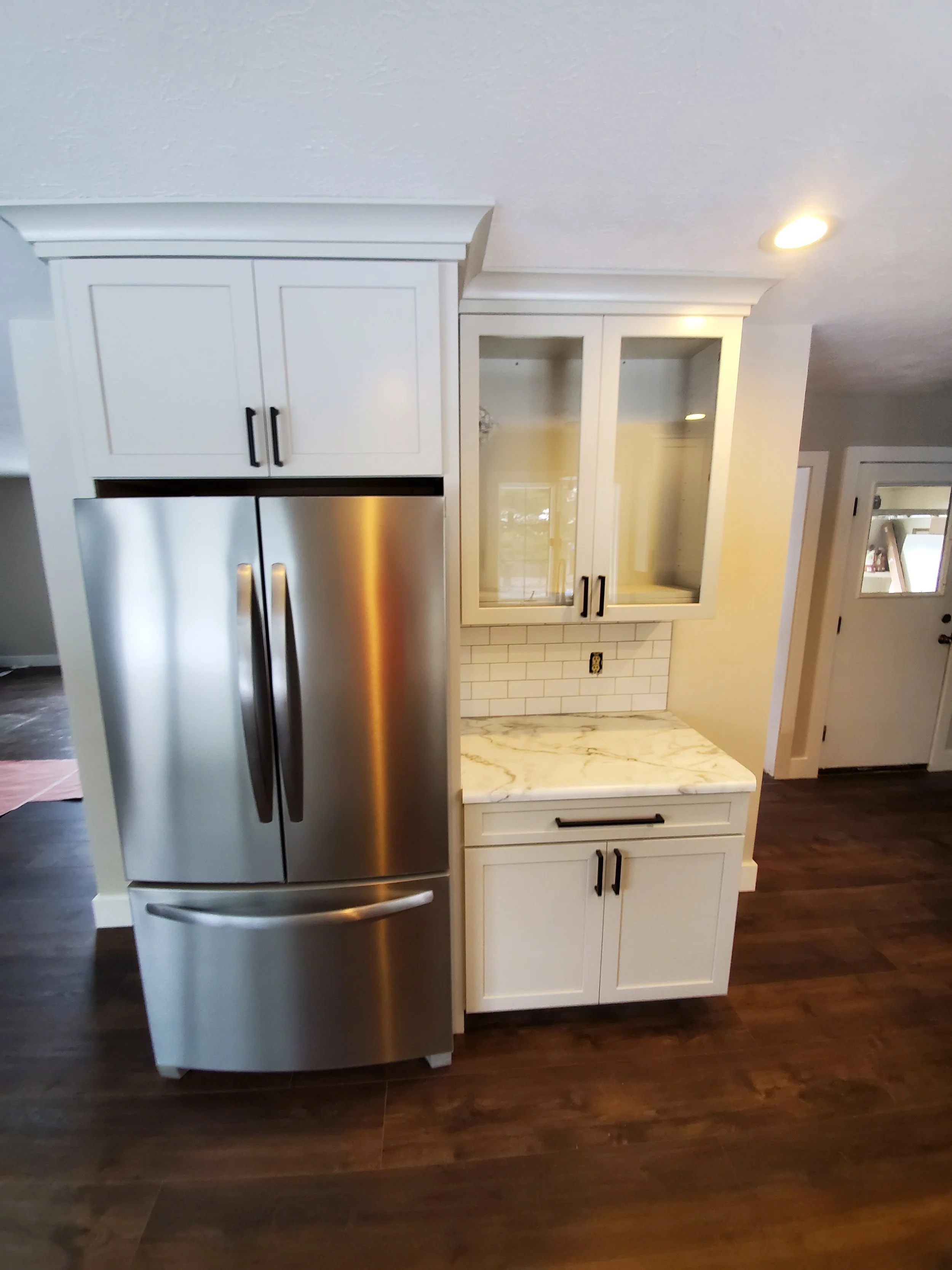 Kitchen remodel with added storage and style, including stainless steel refrigerator and a glass-door upper cabinet above a marble-look countertop.