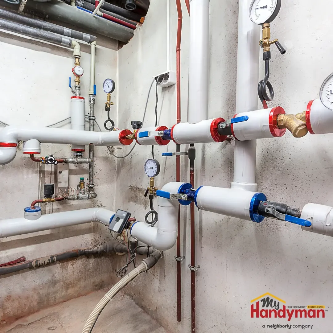 Residential plumbing system with white pipes, red and blue shutoff levers, and pressure gauges mounted on a basement wall in a Washtenaw County, Michigan home.