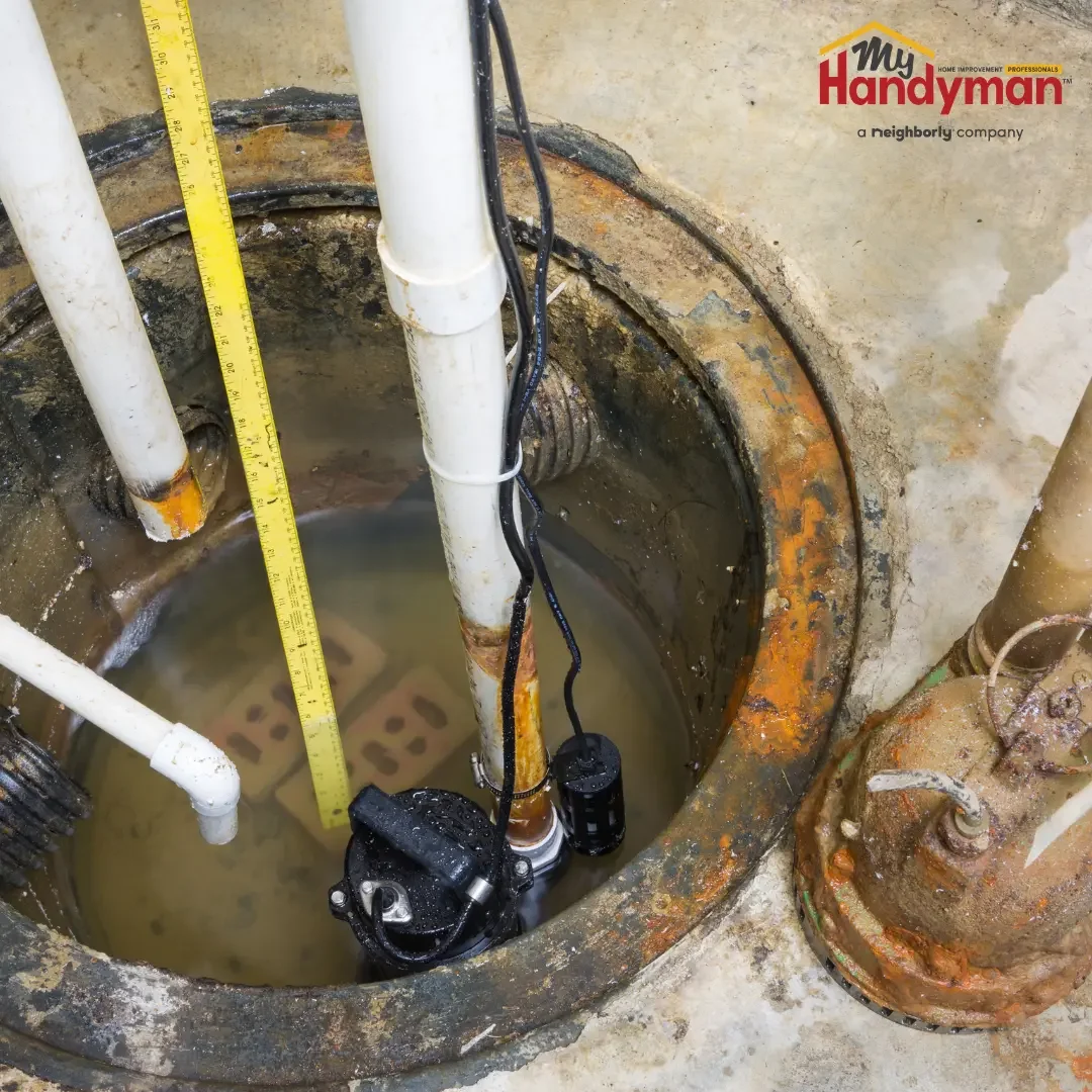 Black submersible sump pump sitting in a sump pit with discharge piping and a tape measure showing water level in a basement near Ann Arbor, Northern Michigan
