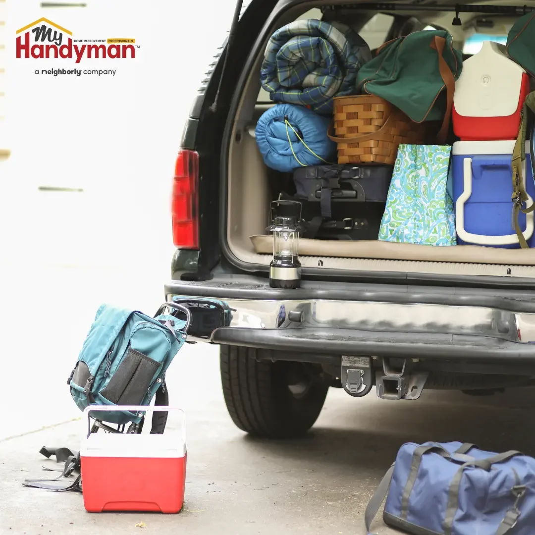 SUV with its rear hatch open and packed with coolers, sleeping bags, and camping gear in a driveway, illustrating summer travel prep for an Ann Arbor, Michigan home.