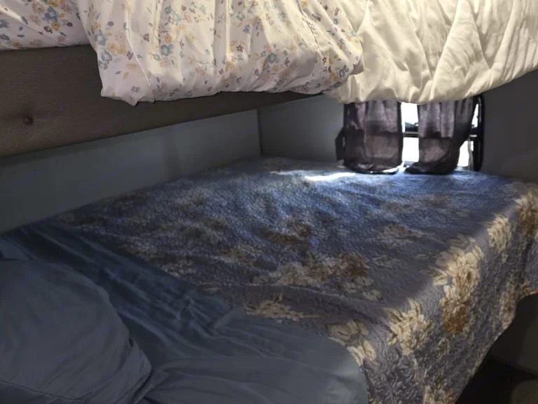 Bottom bunk bed with quilted blanket and a pillow, window with curtains above the bed.