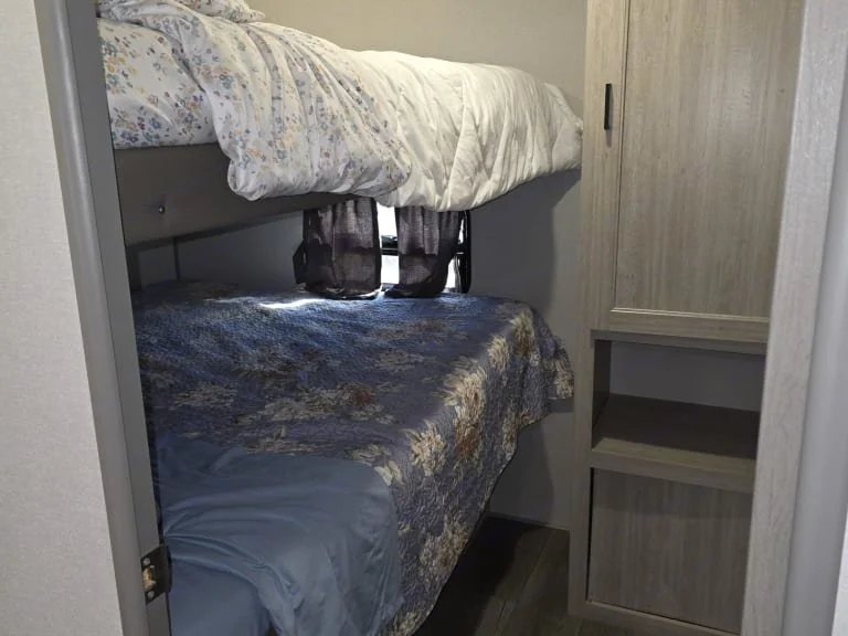 Bunk beds in a small room with a window in between, covered with bedding and a small cabinet on the right