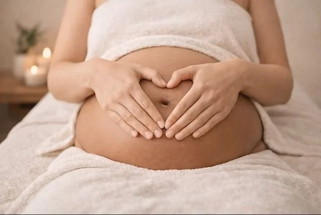 Close-up of a pregnant woman's belly with her hands forming a heart shape over her abdomen.