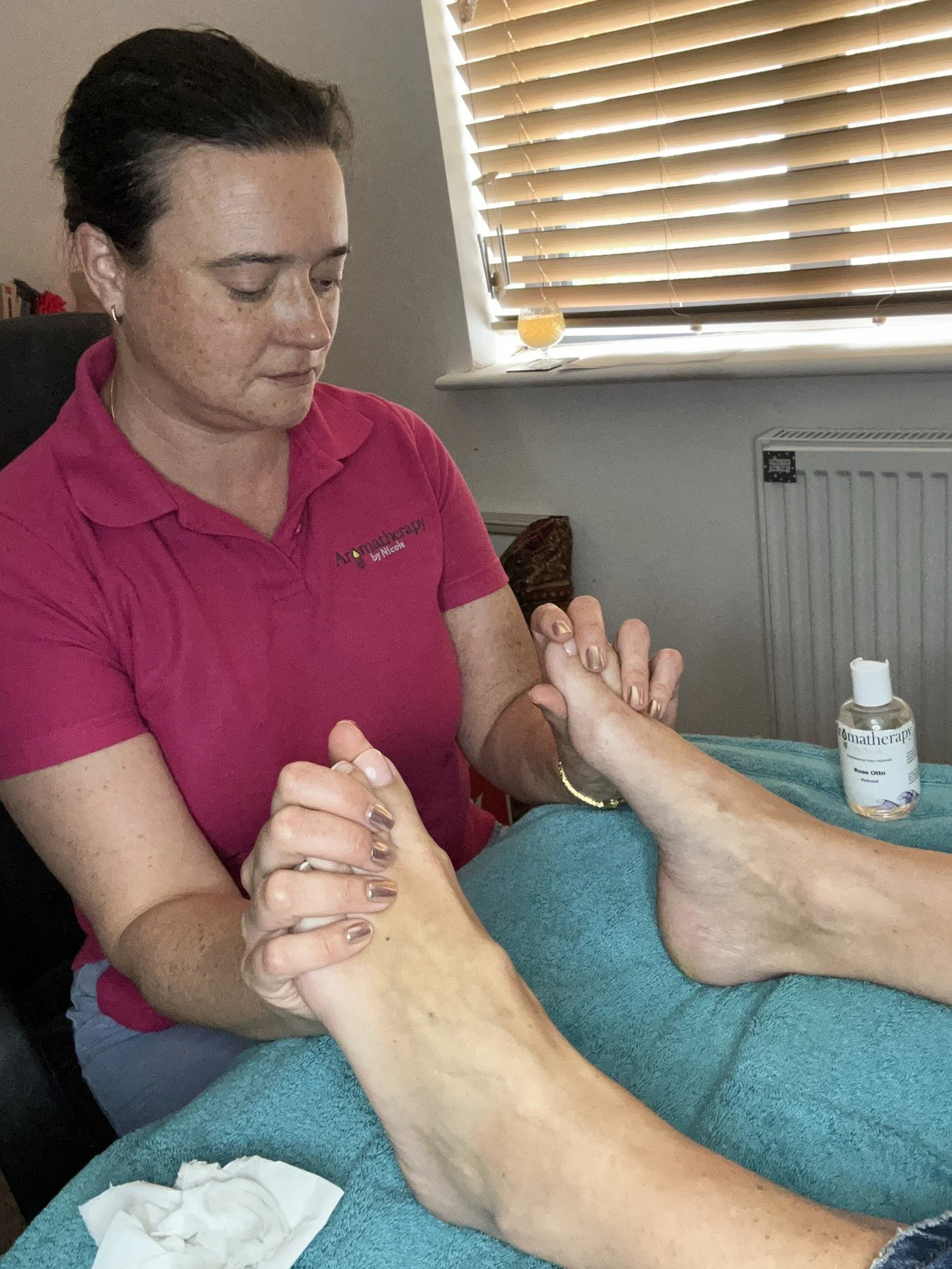 A woman giving a hand massage to an elderly person's hand at a therapy session, with a bottle of aromatherapy massage oil on the table.