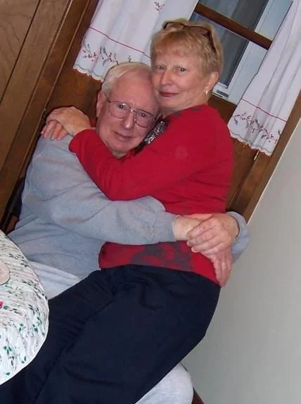 Kate's parents embracing and smiling together indoors.