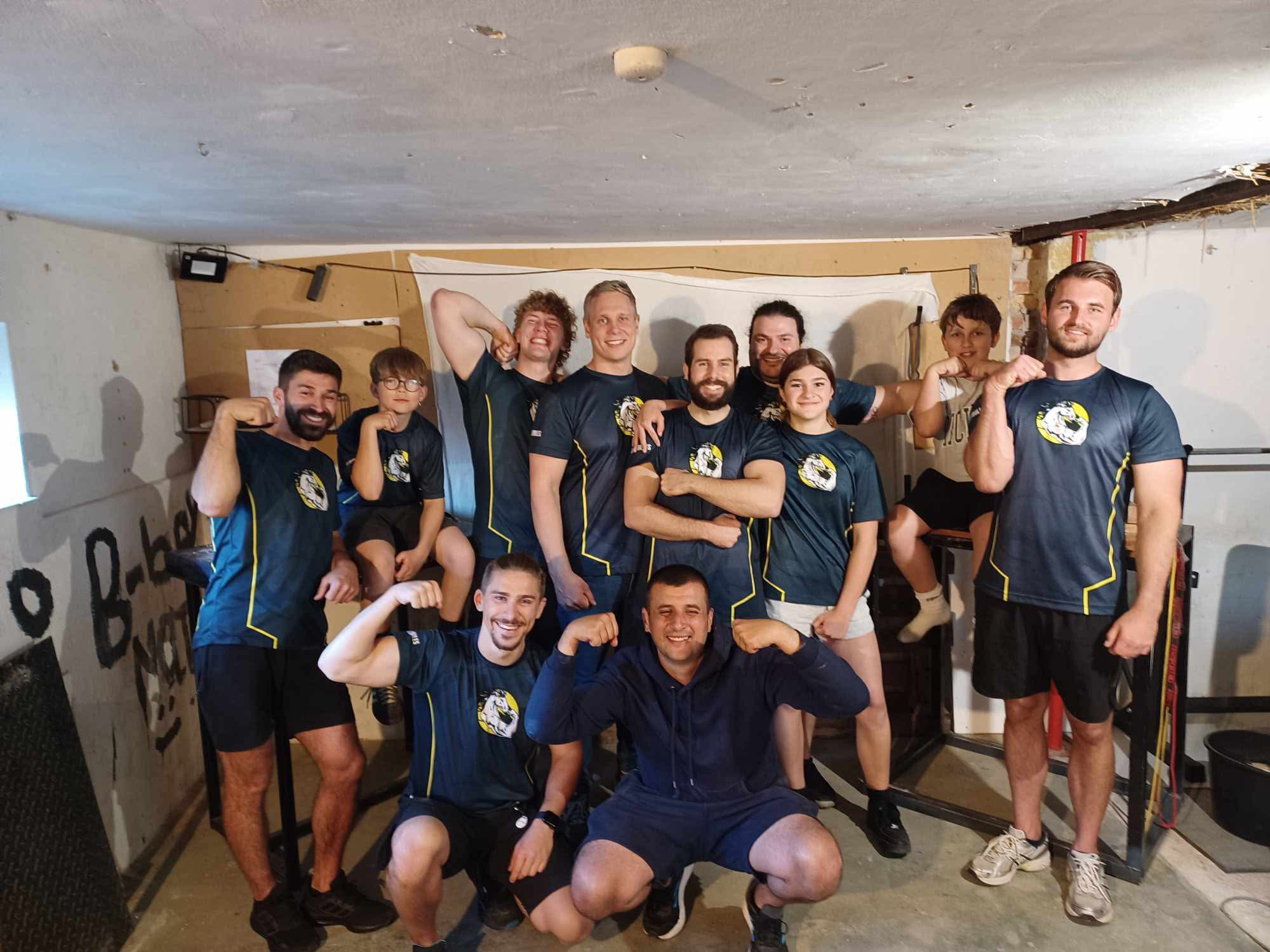 En gruppe sportsudøvere iført matchende t-shirts, der poser for kameraet i et indendørs træningslokale.