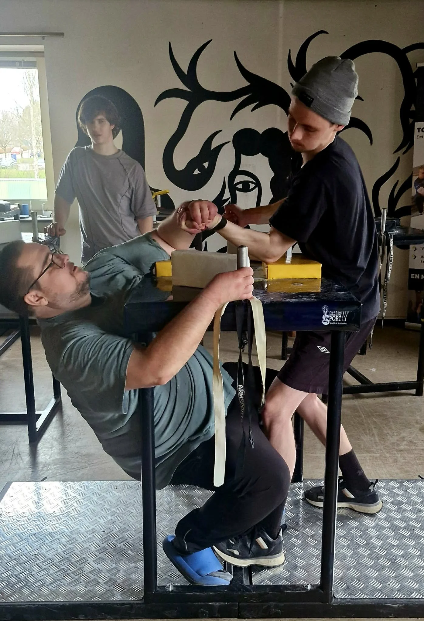 To mænd, der træner kampsport, med en yngre dreng, der holder en håndsving, i et fitnesscenter.
