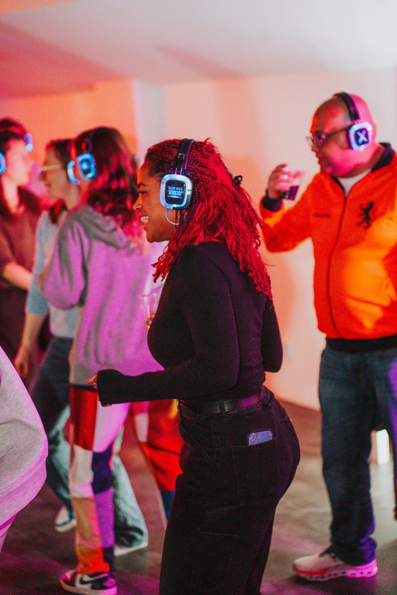 Mensen dansen op een feestje met neonverlichting, iedereen draagt koptelefoons.