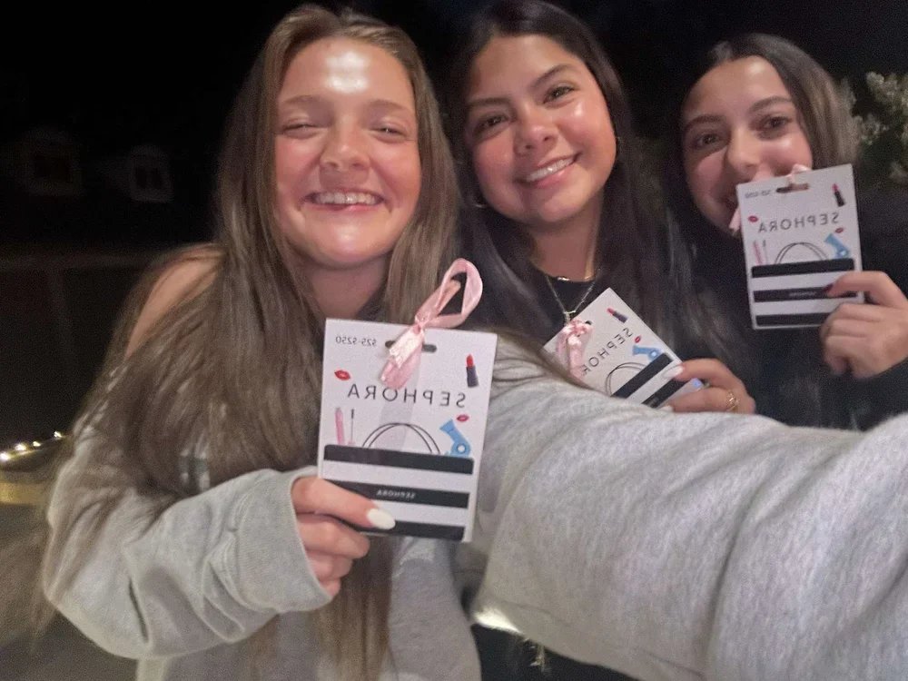 Three young women smiling and taking a selfie at night, each holding a Sephora gift card.