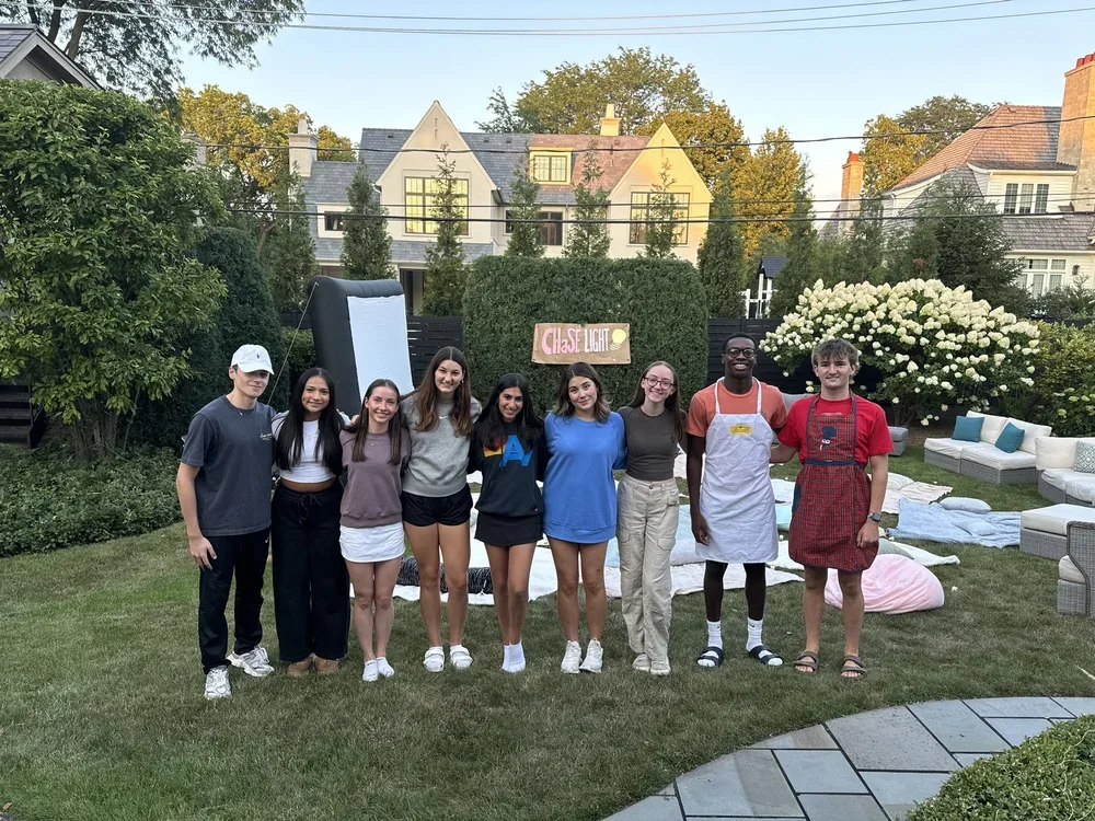 Group of nine young people standing outdoors in a backyard with a
