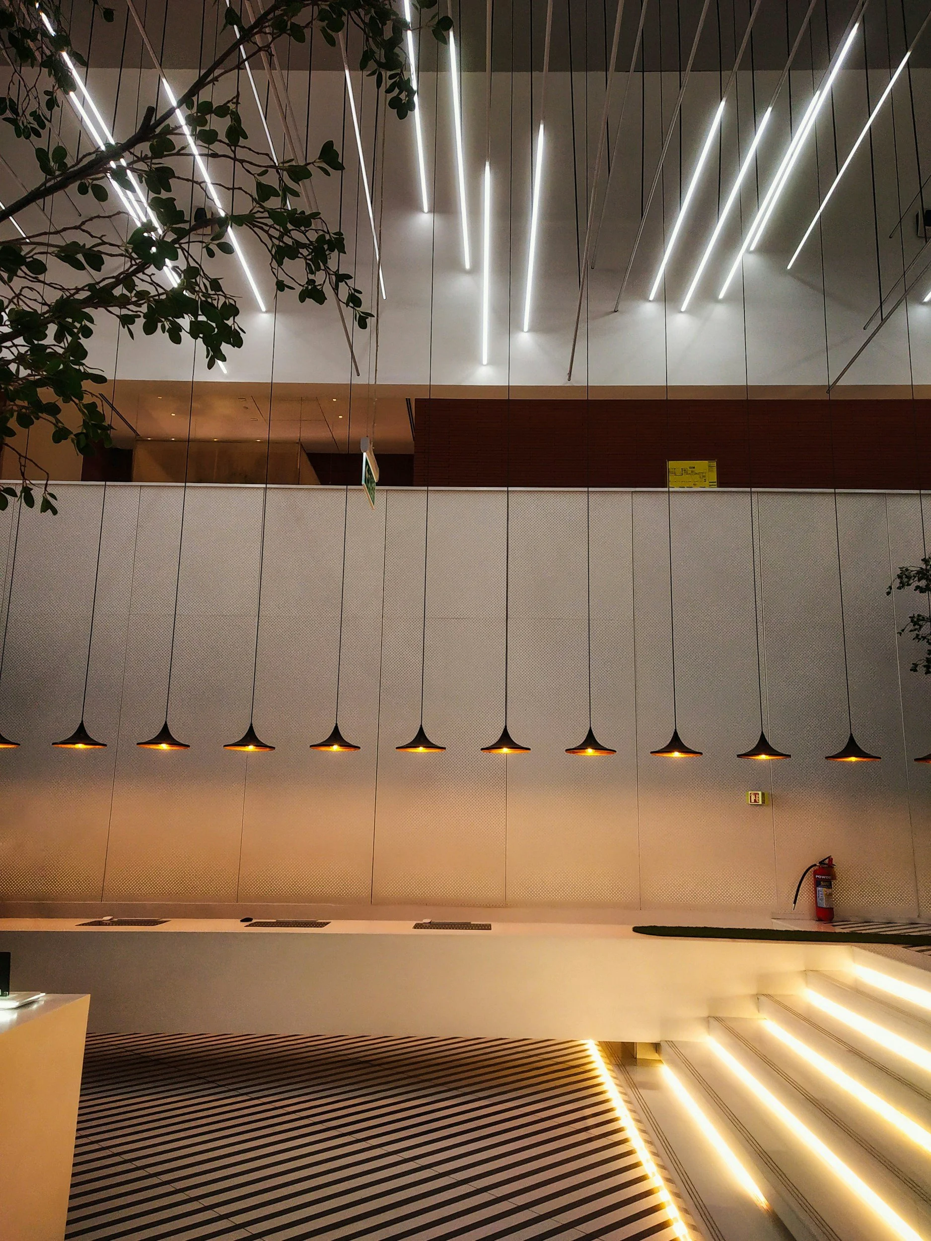 Interior of a modern building with aesthetic lighting, a patterned floor, and stairs on the right side.